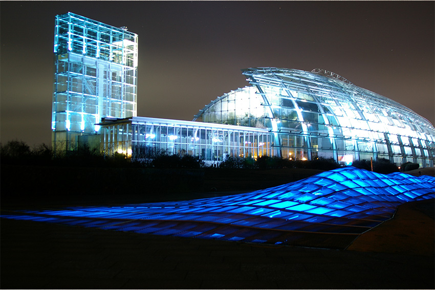 Aquamarine Fukushima: gläserne Architektur bei Nacht Nachtaufnahme des Aquamarine Fukushima mit moderner Glasarchitektur und blau beleuchtetem Vorplatz