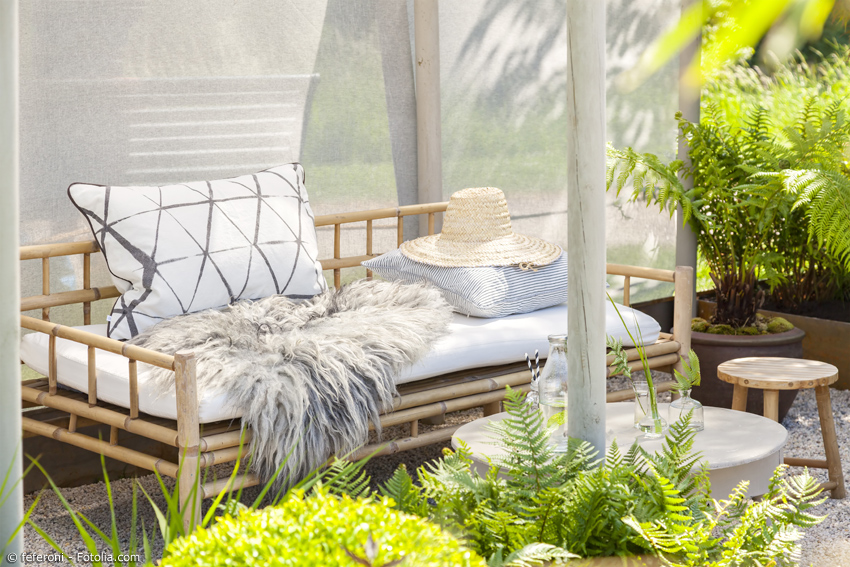 Bambusmöbel mit Kissen auf einer Veranda, umgeben von Grünpflanzen
