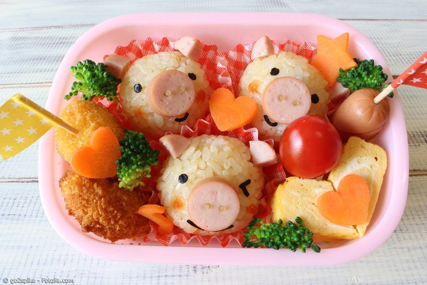 Reis und Würstchen Scheiben in Form von Schweinen mit ausgestochenen Karottenherzen und Pieksern