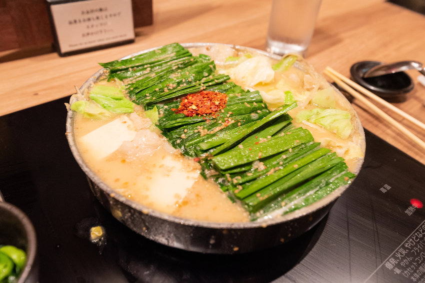 Motsunabe Spezialität in Fukuoka Ein dampfender Topf Motsunabe-Eintopf mit reichlich Lauch, Tofu und Chili, serviert auf einer Herdplatte im Restaurant.