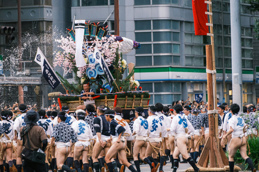 Hakata Gion Yamakasa Festival in Fukuoka Männer in traditioneller Festkleidung tragen einen kunstvoll geschmückten Festwagen beim Hakata Gion Yamakasa Matsuri durch die Straßen von Fukuoka, während Wasser zur Abkühlung gespritzt wird.
