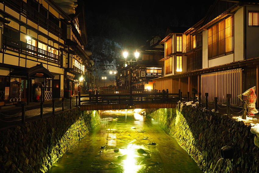 Ginzan Onsen bei Nacht, beleuchtete Ryokan-Gasthäuser am Fluss, historischer Onsen-Ort in Yamagata, Japan