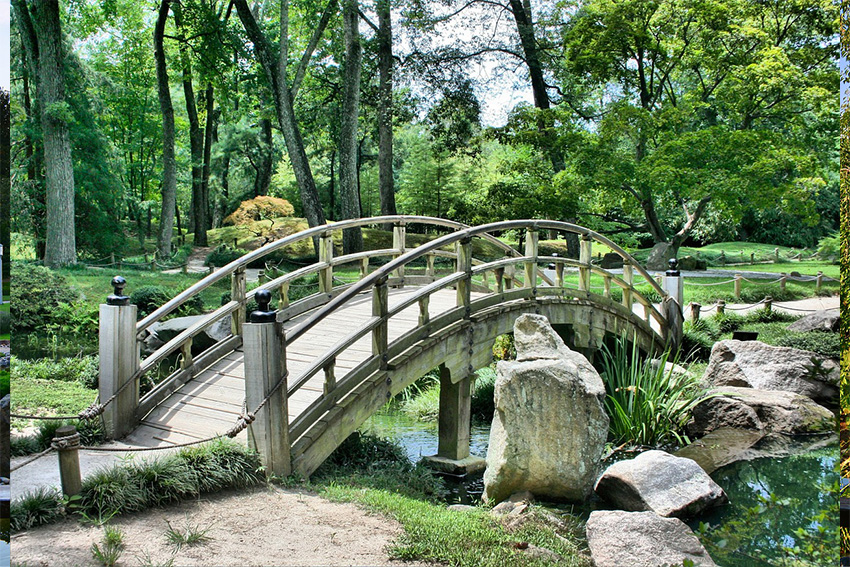 Japanischer Garten mit geschwungener Holzbrücke über einem Bach – Symbol für die Harmonie der Elemente Holz, Wasser und Erde
