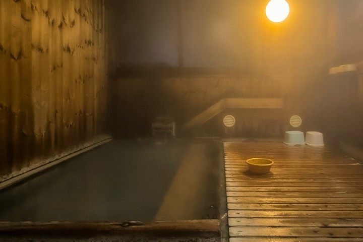 Japanisches Onsen-Bad mit heißem Wasser, Holzboden und Badeeimern als Unterschied zur Sauna