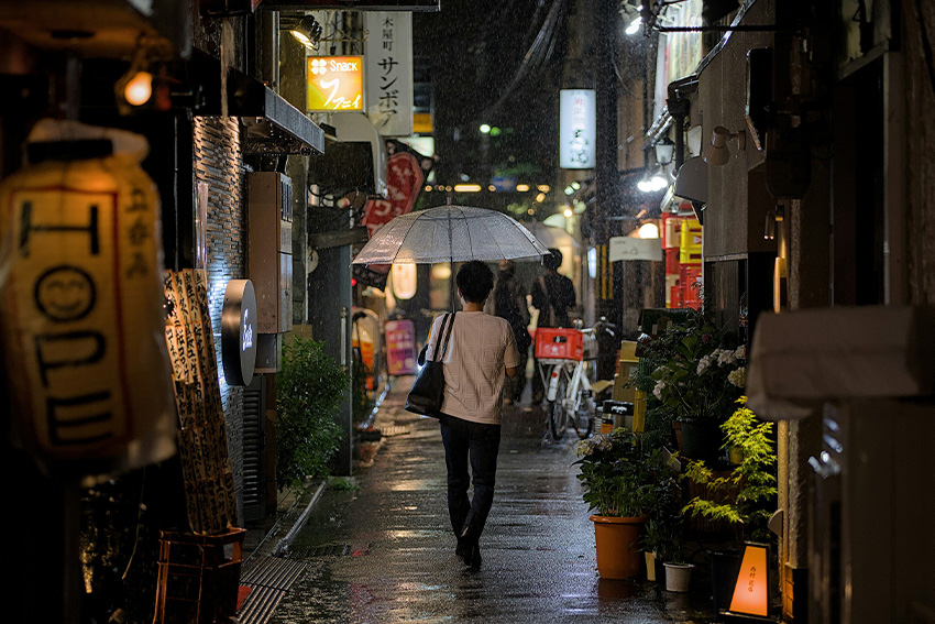 Regnerischer Sommerabend in einer japanischen Gasse mit Person unter durchsichtigem Regenschirm