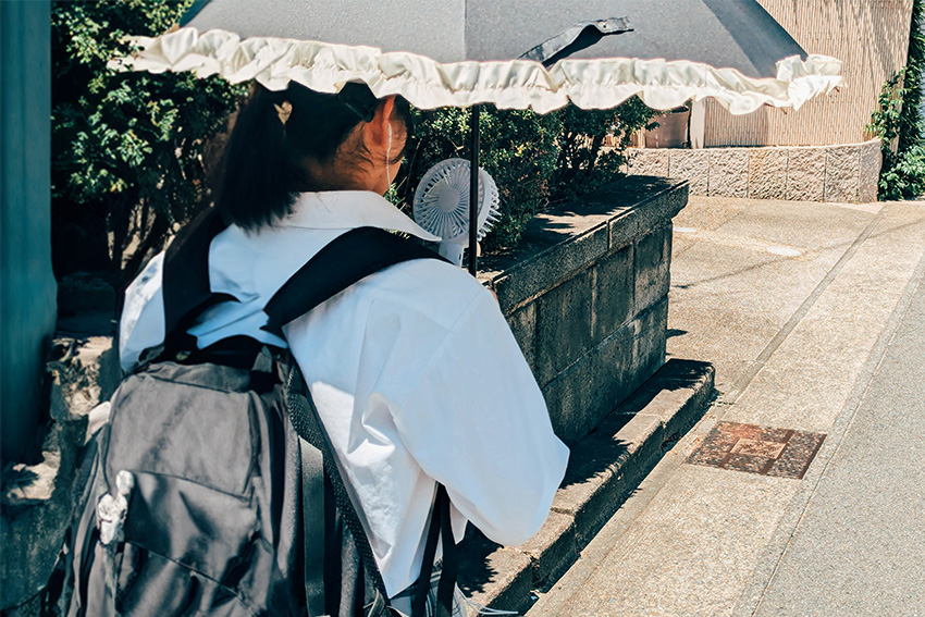 Person mit Sonnenschirm und tragbarem Ventilator an einem heißen Sommertag in Japan
