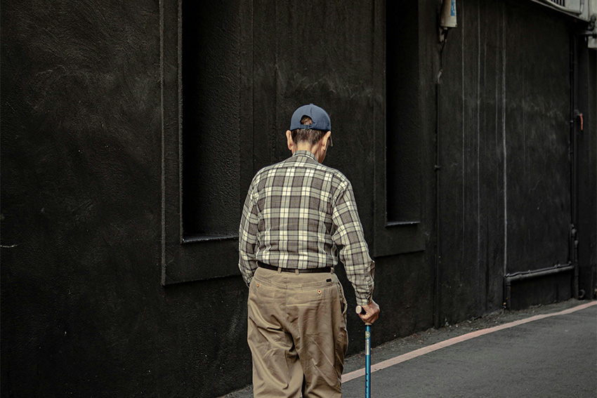 Älterer Mann mit Gehstock in einer engen Straße in Japan – Symbol für Überalterung und soziale Isolation