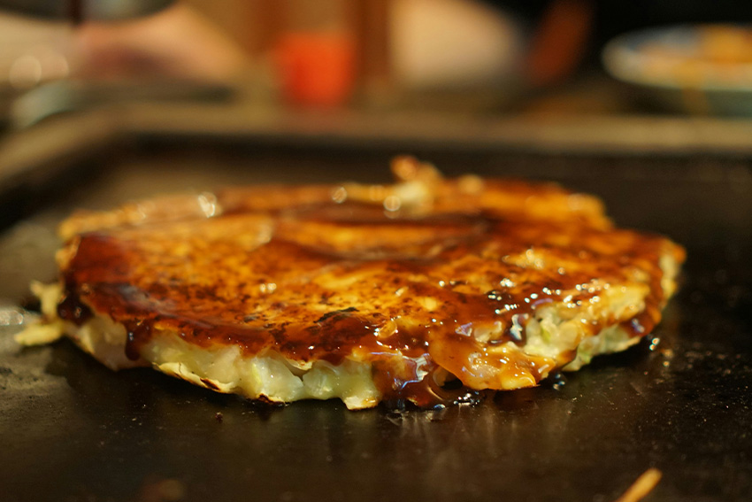Veganes Okonomiyaki, japanischer Kohlpfannkuchen mit dunkler Soße, frisch gebraten auf der Grillplatte