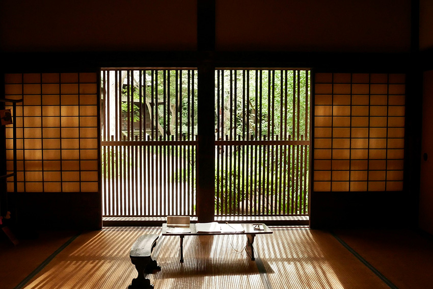 Japanischer Tatami-Raum mit Shoji, Holzlamellen, Schatten und Blick ins Grüne
