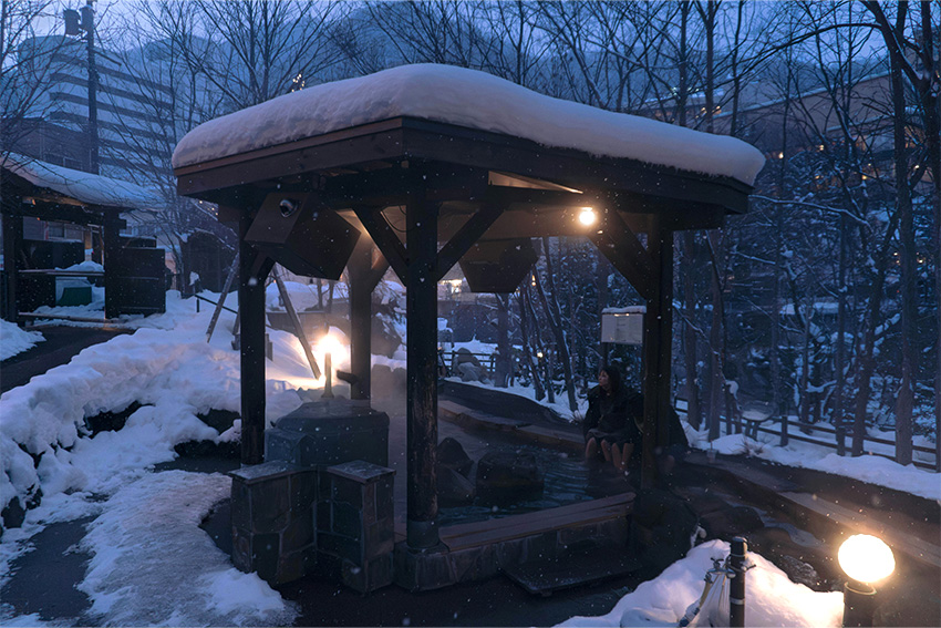 Jozankei Onsen Fußbad im Winter mit überdachtem Ashiyu, Schnee, warmem Wasser und abendlicher Stimmung nahe Sapporo