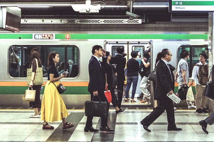 Bahnfahren in Japan: Orientierung mit Linien, Farben und Stationen Reisende an einem japanischen Bahnsteig vor einem Zug mit Linienfarbe und Stationsschild in Shibuya