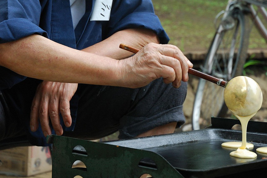 Dorayaki Teig wird mit einer Kelle auf einer heißen Eisenplatte ausgegossen