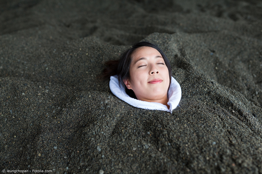 Frau entspannt im dunklen Sand, eingegraben bis zum Hals