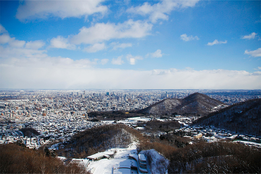 Panoramablick vom Mt. Moiwa auf Sapporo im Win-ter mit verschneiten Hügeln und dicht bebautem Stadtgebiet