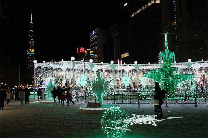Sapporo White Illumination im Odori Park bei Nacht mit leuchtenden Lichtinstallationen, Besuchern im Schnee und dem Sapporo TV Tower im Hinter-grund