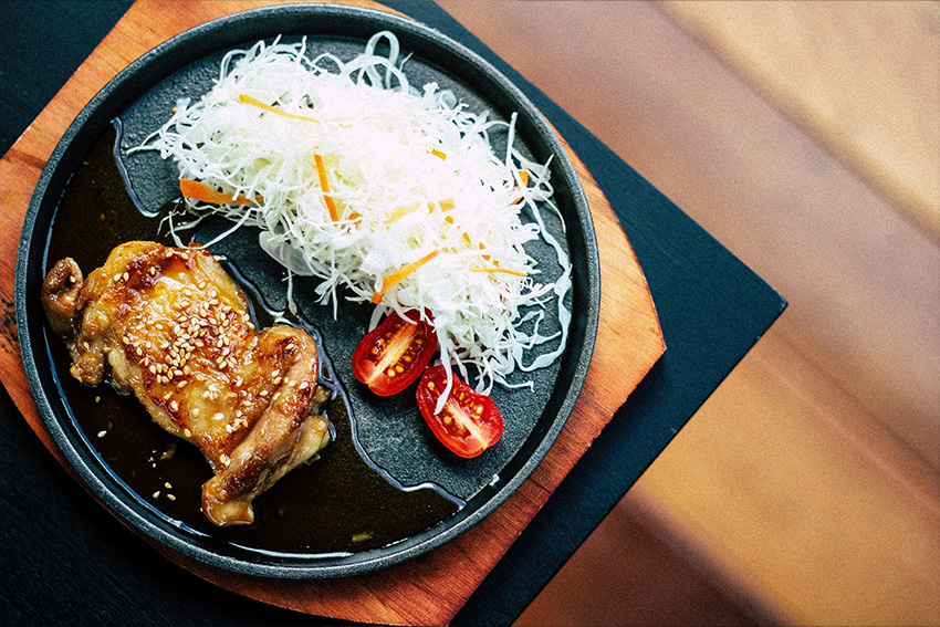 Schnelles Teriyaki Hähnchen mit Sesam, feinem Salat und Kirschtomaten auf einer schwarzen Platte serviert