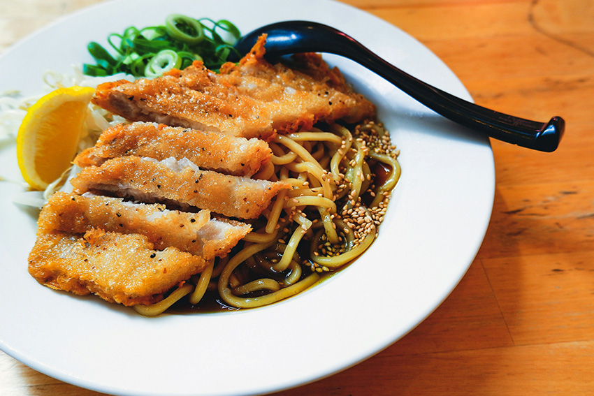 Goldbraun paniertes Tonkatsu mit Nudeln, Sauce, Frühlingszwiebeln und Zitrone – belieb-tes japanisches Wohlfühlgericht