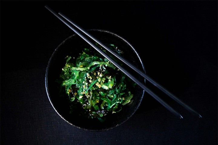 Schüssel mit japanischem Wakame-Algensalat, garniert mit Sesam und Stäbchen – veganes Gericht mit Umami-Geschmack