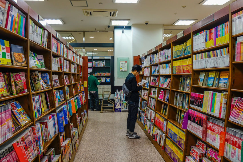 Besucher einer japanischen Buchhandlung liest im Stehen zwischen hohen Bücherregalen – ein Beispiel für das japanische Wort Tachiyomi
